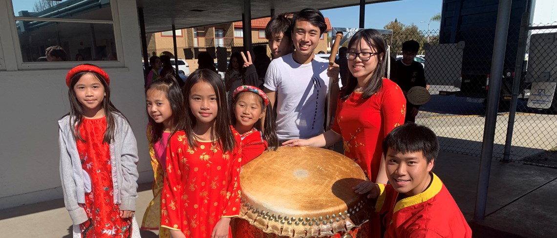Students wearing traditional TET garb around a drum.